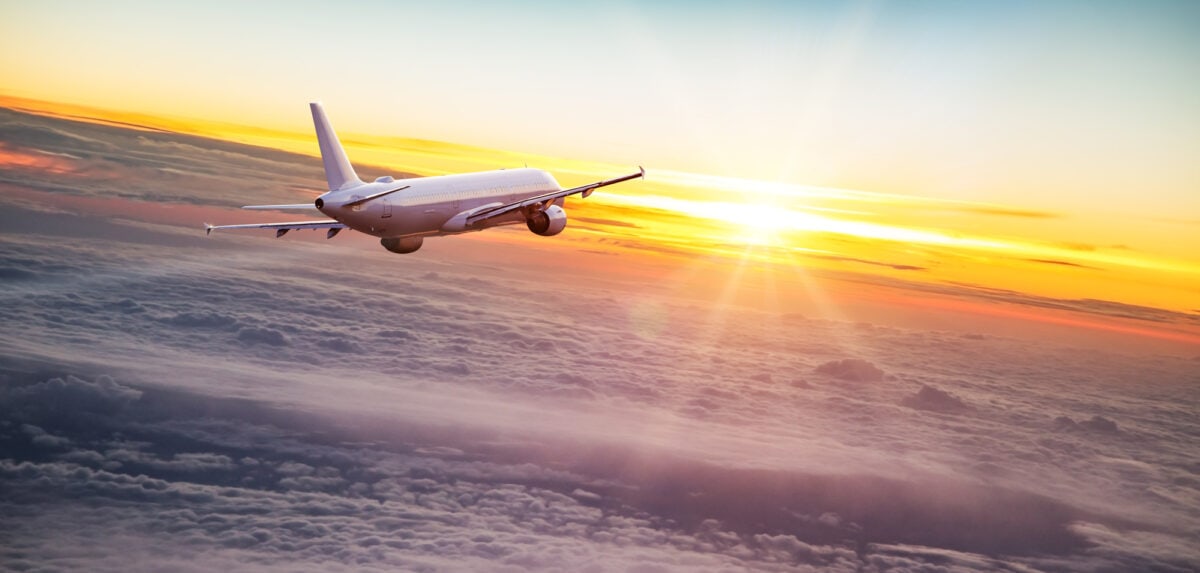 plane flying towards sun over clouds